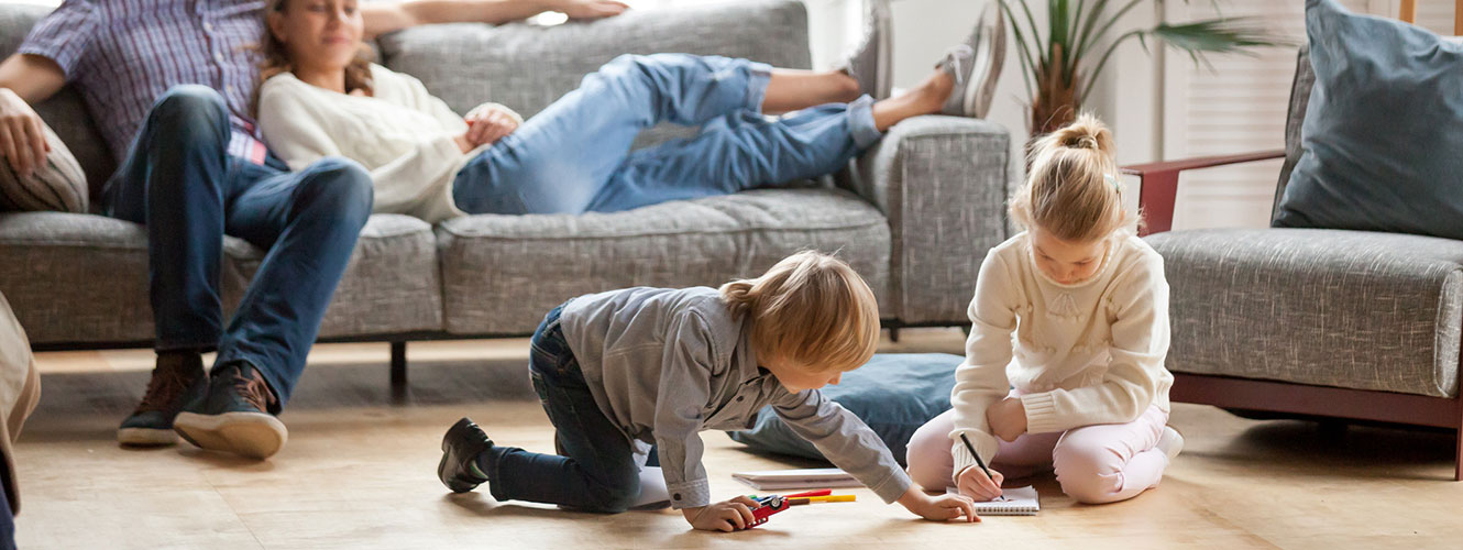 Two kids playing in living room while parents watch